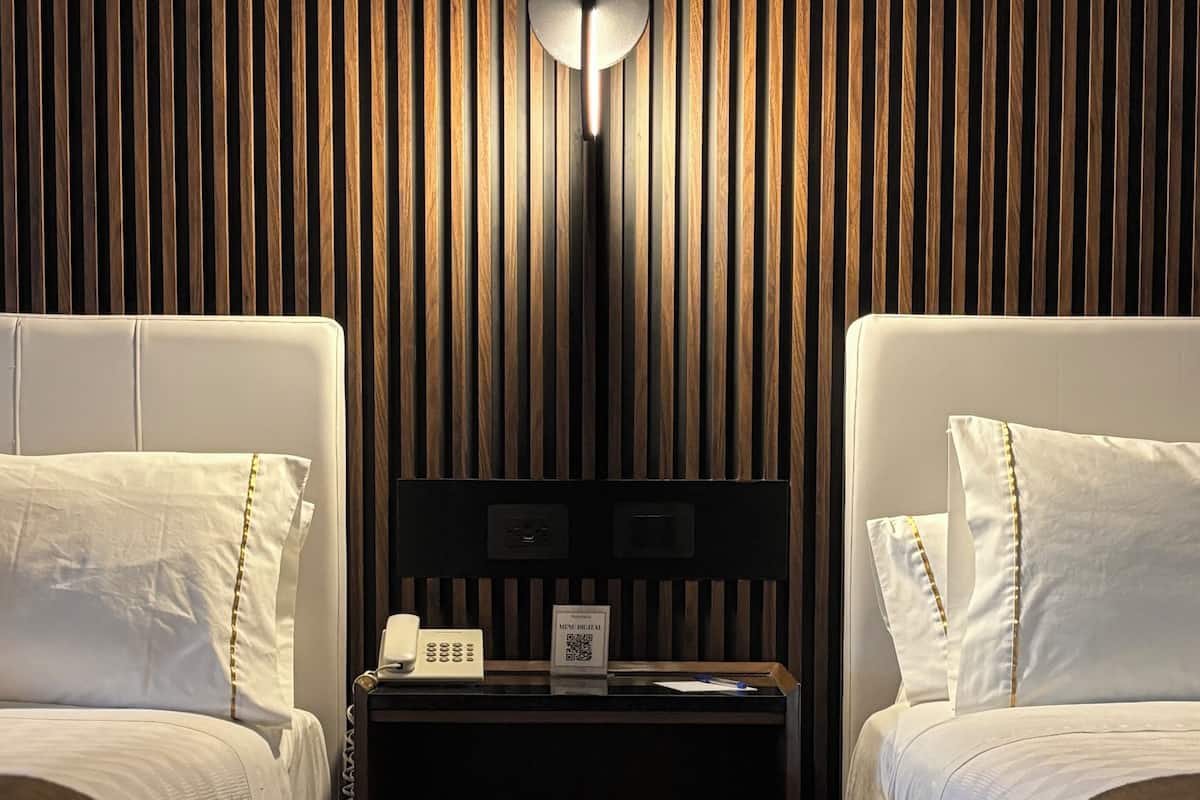 A hotel room with two beds, a nightstand, a wall-mounted lamp, and a QR code on the nightstand.