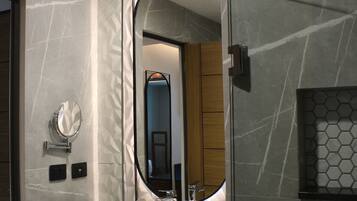 Un baño moderno con un espejo grande, un lavamanos blanco y una pared de mármol.