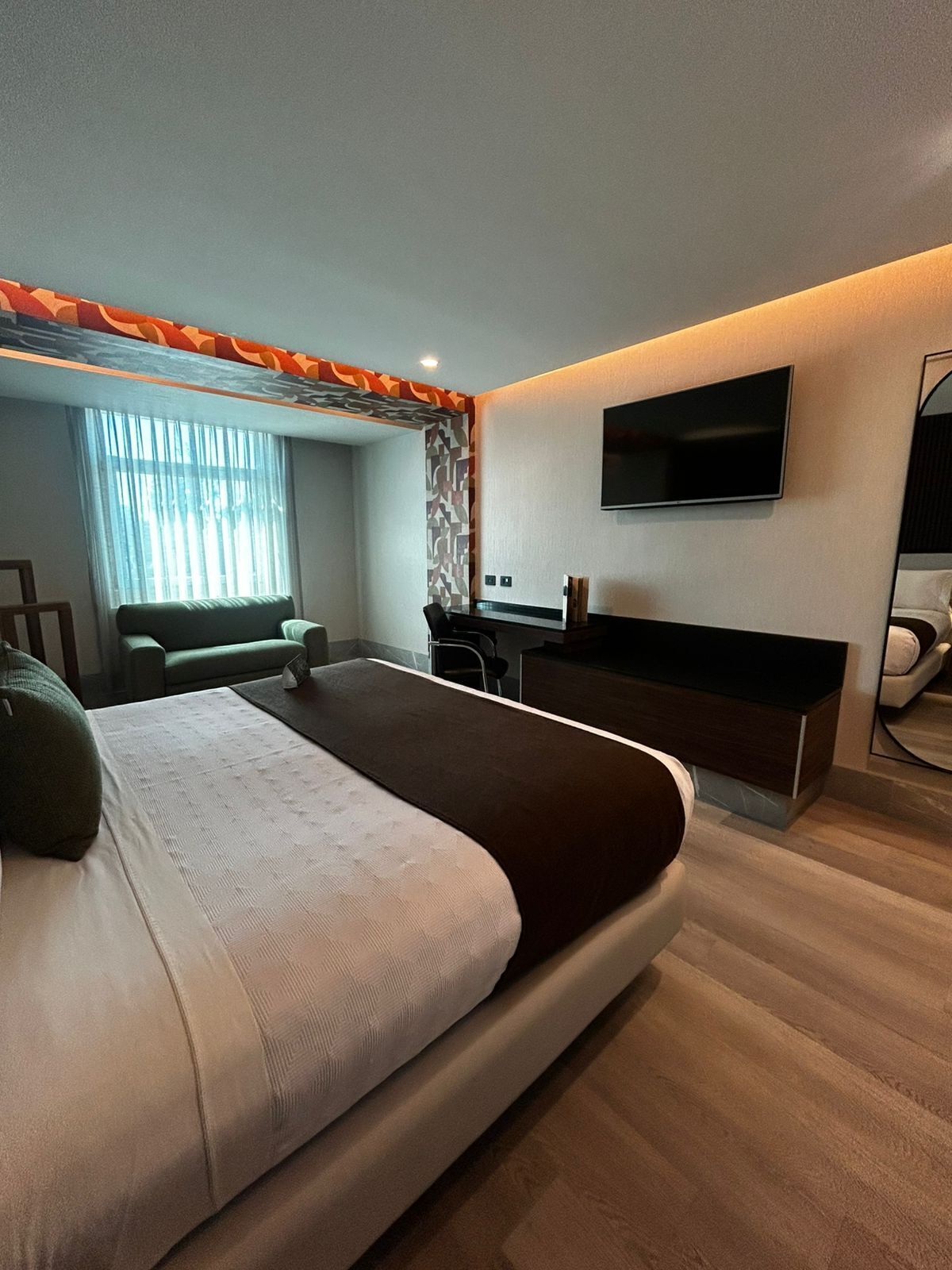 A modern bedroom with a large bed, a desk, a chair, a TV, and a window with curtains.