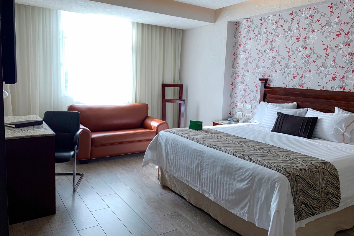 A hotel room with a bed, a desk, a chair, and a window with curtains.
