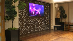 Una sala de estar moderna con un televisor de pantalla plana montado en una pared decorativa, piso de madera y una planta en maceta.