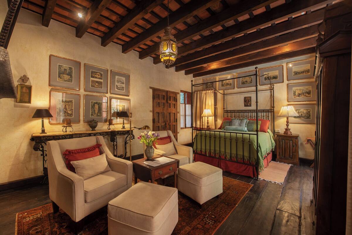 A traditional room with a bed, two armchairs, a small table, and a nightstand.