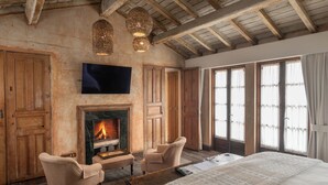 A bedroom with a large bed, a fireplace, wooden walls, and a TV mounted above it. - Hotel Posada del Angel (Antigua Guatemala)
