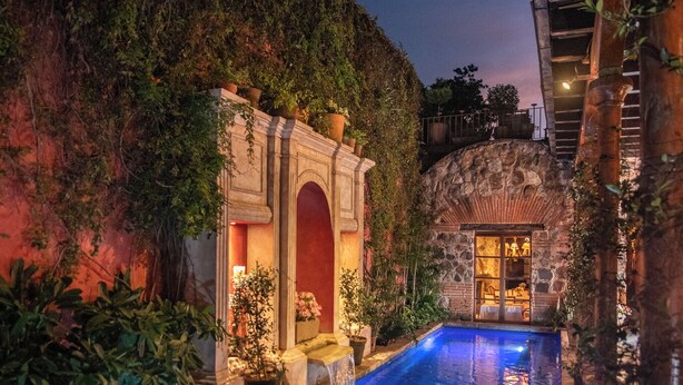 A pool area with a stone archway, a small waterfall, and a view of a building with a balcony. - Hotel Posada del Angel (Antigua Guatemala)