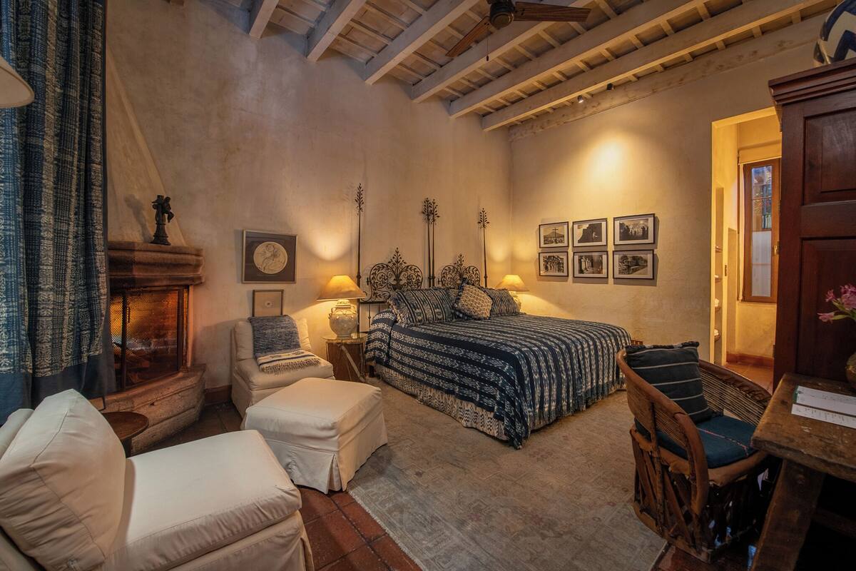 A cozy bedroom with a bed, two chairs, a small table, and a fireplace.