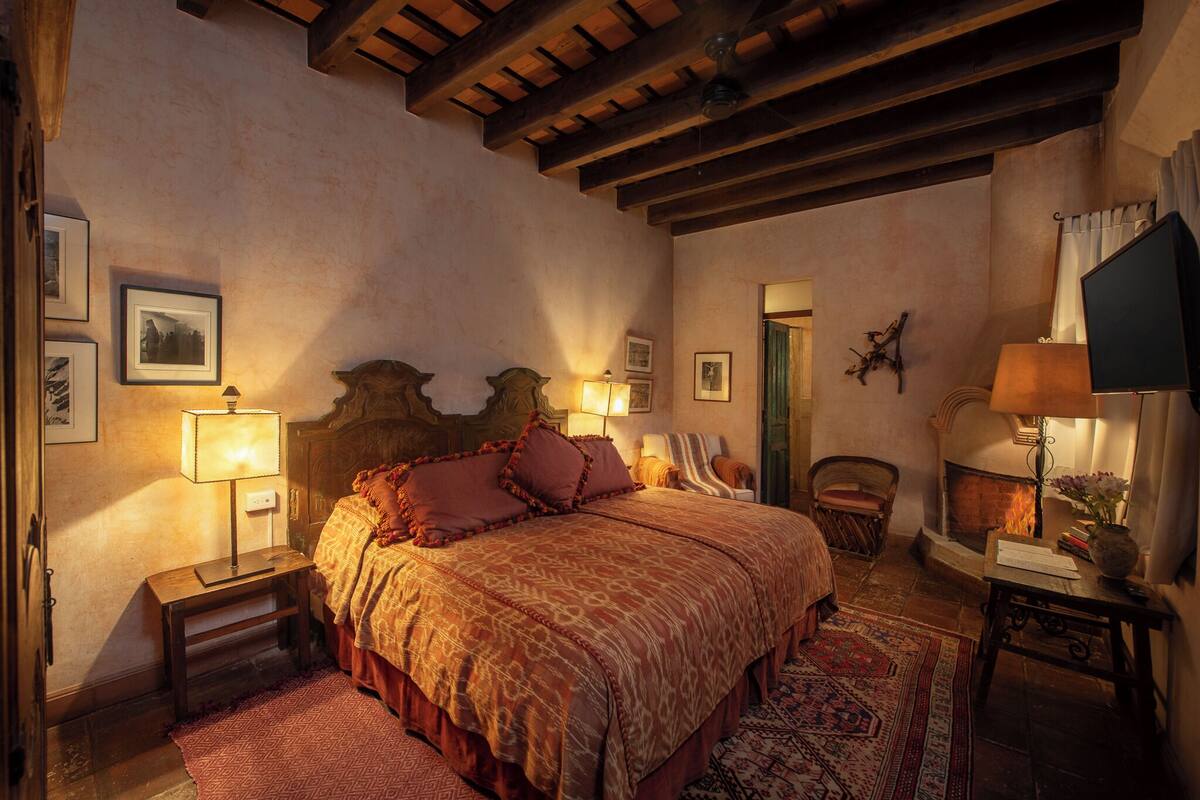 A traditional bedroom with a large bed, wooden beams, a fireplace, and a cozy atmosphere.