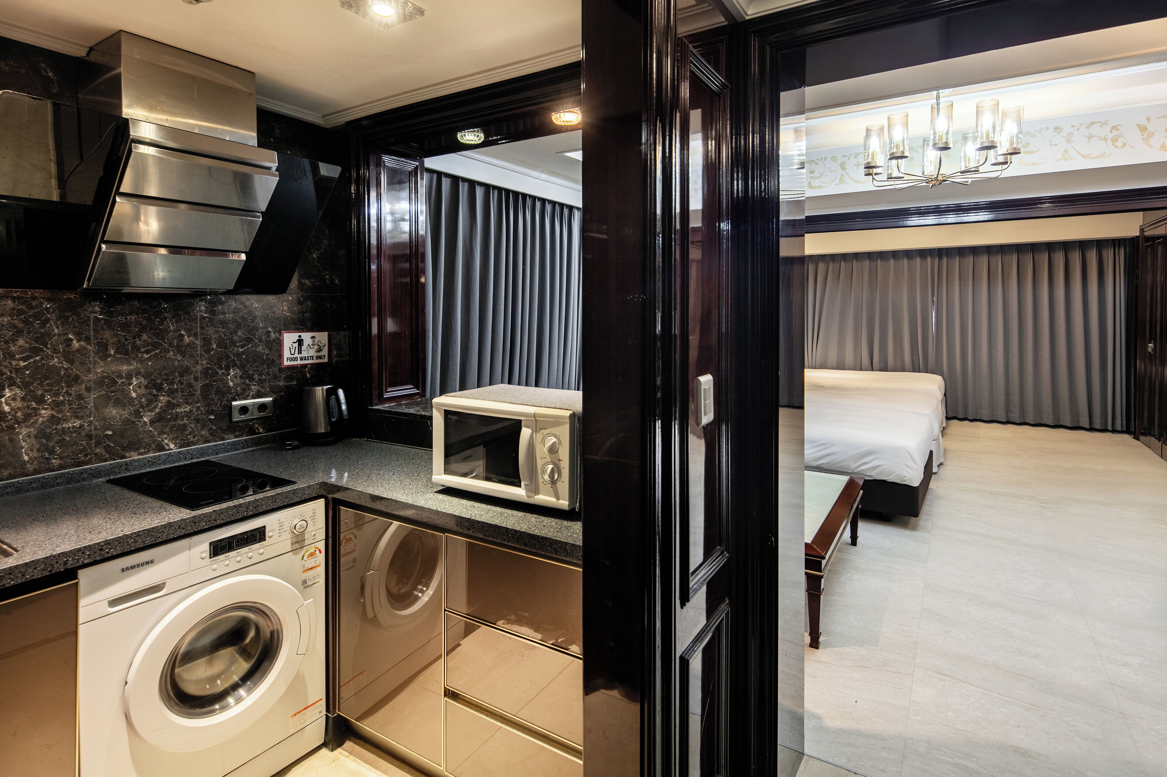 Une chambre d’hôtel compacte équipée d’une kitchenette, d’un lave-linge, d’un four à micro-ondes, d’un lit et d’une grande fenêtre.
