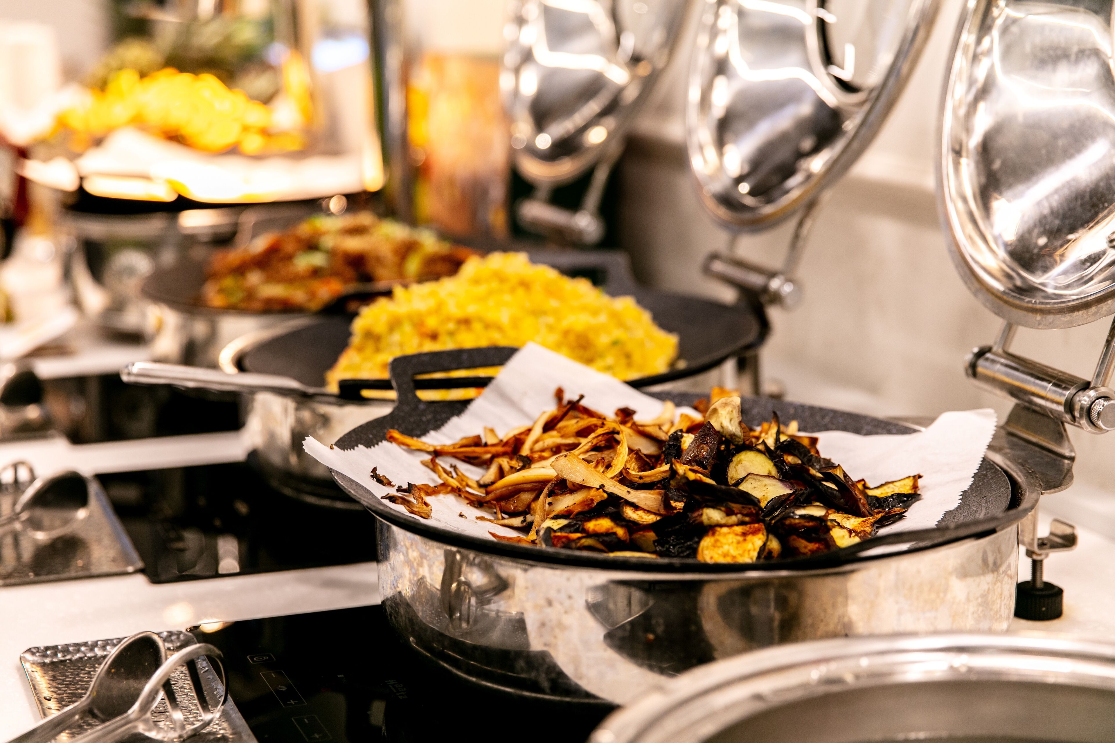 Un buffet proposant divers plats, notamment des oignons frits et du riz jaune, servis dans des récipients en métal.
