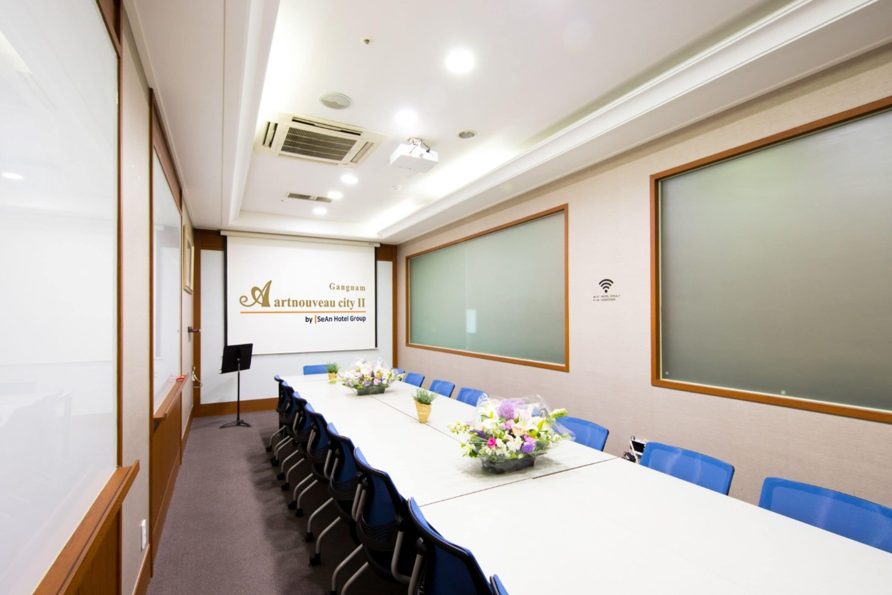 Un salón de conferencias con una larga mesa, sillas azules y centros de mesa con flores.