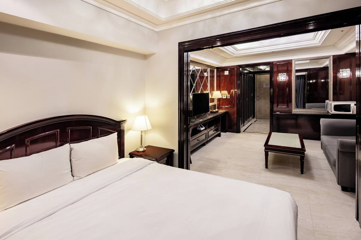 Ein Hotelzimmer mit einem großen Bett, einem Schreibtisch mit Lampe, einem Fernseher, einer Mikrowelle und einer Sitzecke.