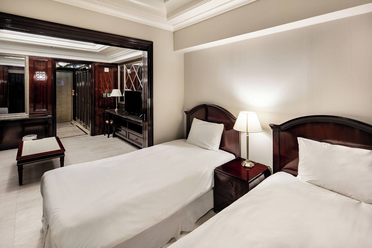 Ein Hotelzimmer mit zwei Betten, einem Schreibtisch, einem Schminktisch, einem Spiegel und einem Fernseher.