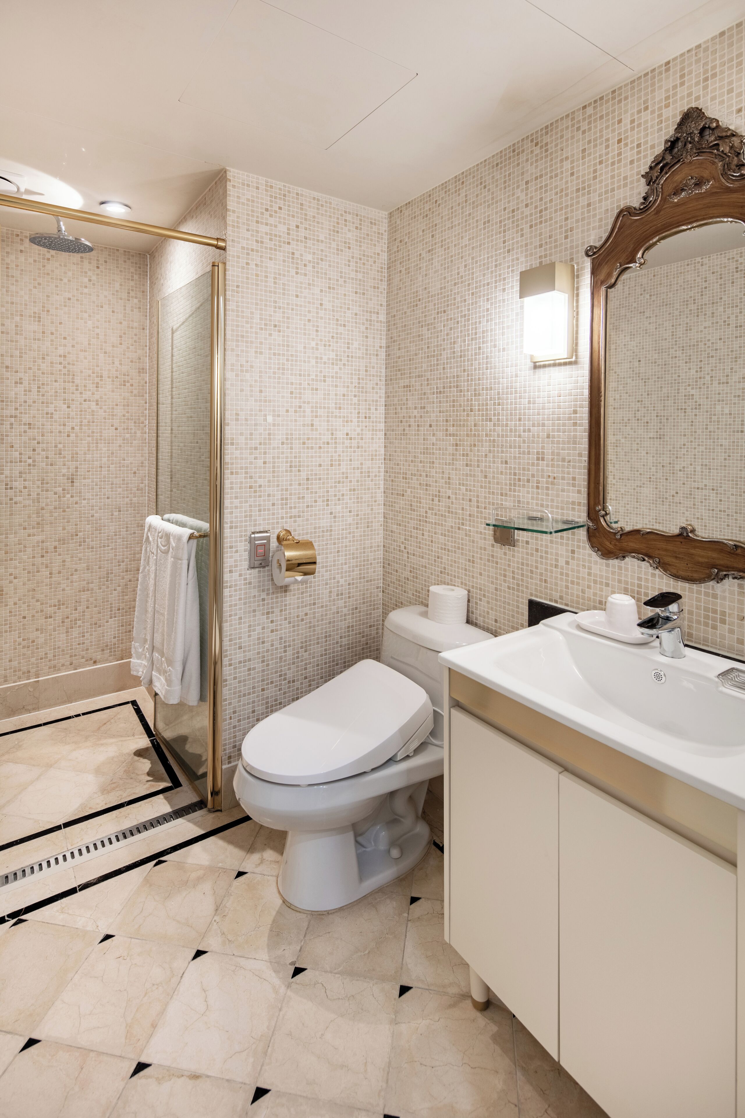 Un baño moderno con cabina de ducha de vidrio, inodoro blanco, lavabo con espejo y suelo de baldosas.