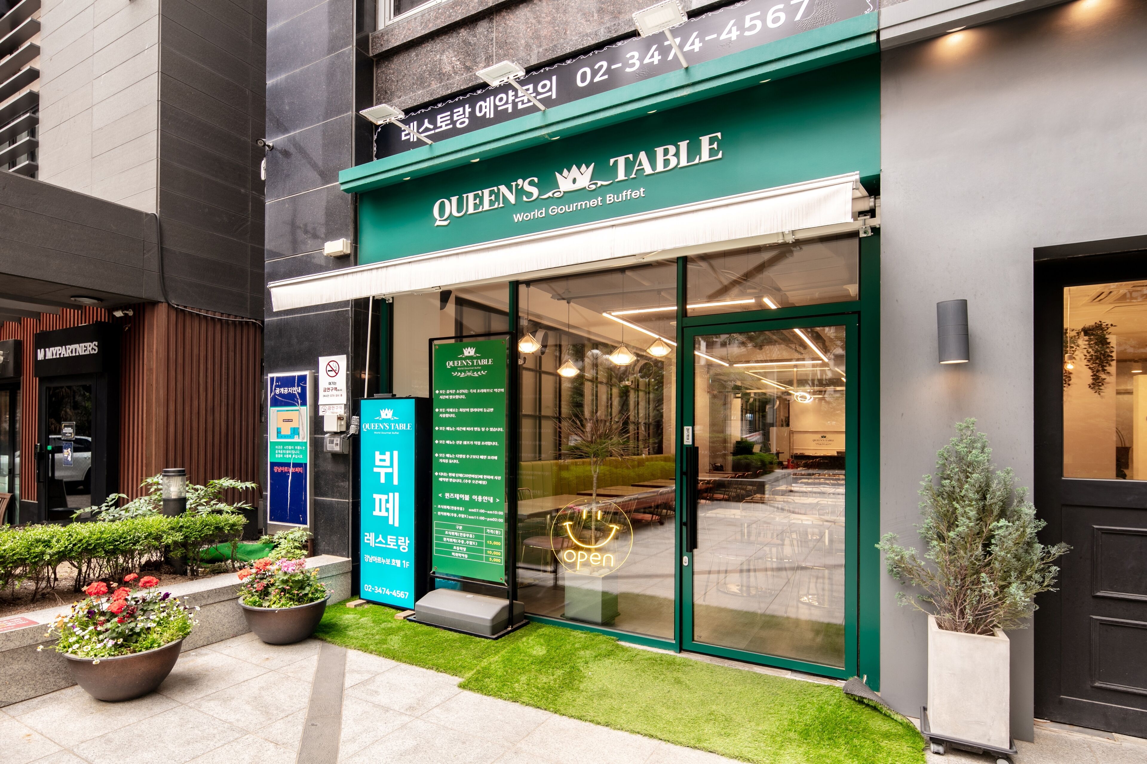 Ein Restaurant mit grünem Markisenvorzelt, Glastür und Außenbereich mit Topfpflanzen.