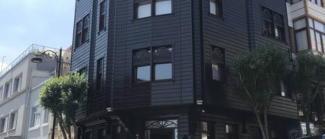 A multi-story building with a dark facade, a central entrance with steps, and a small garden area with potted plants.