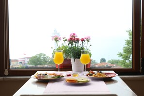 A breakfast table with plates of food, two glasses of orange juice, and a potted plant by a window with a view of buildings and a flag. - Emine Sultan Hotel (Istanbul)