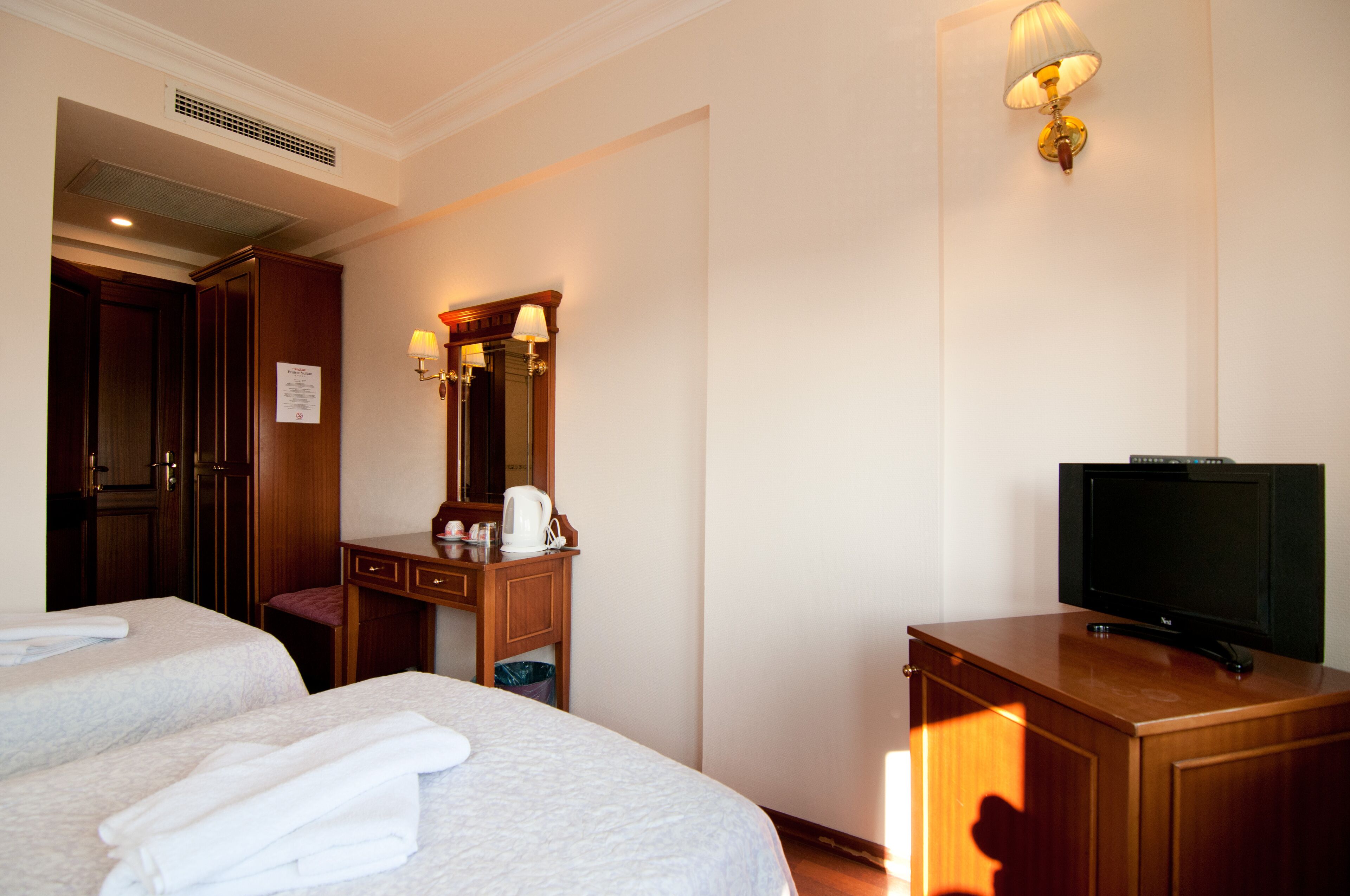 A hotel room with two beds, a wooden dresser, a television, and a mirror with wall sconces.