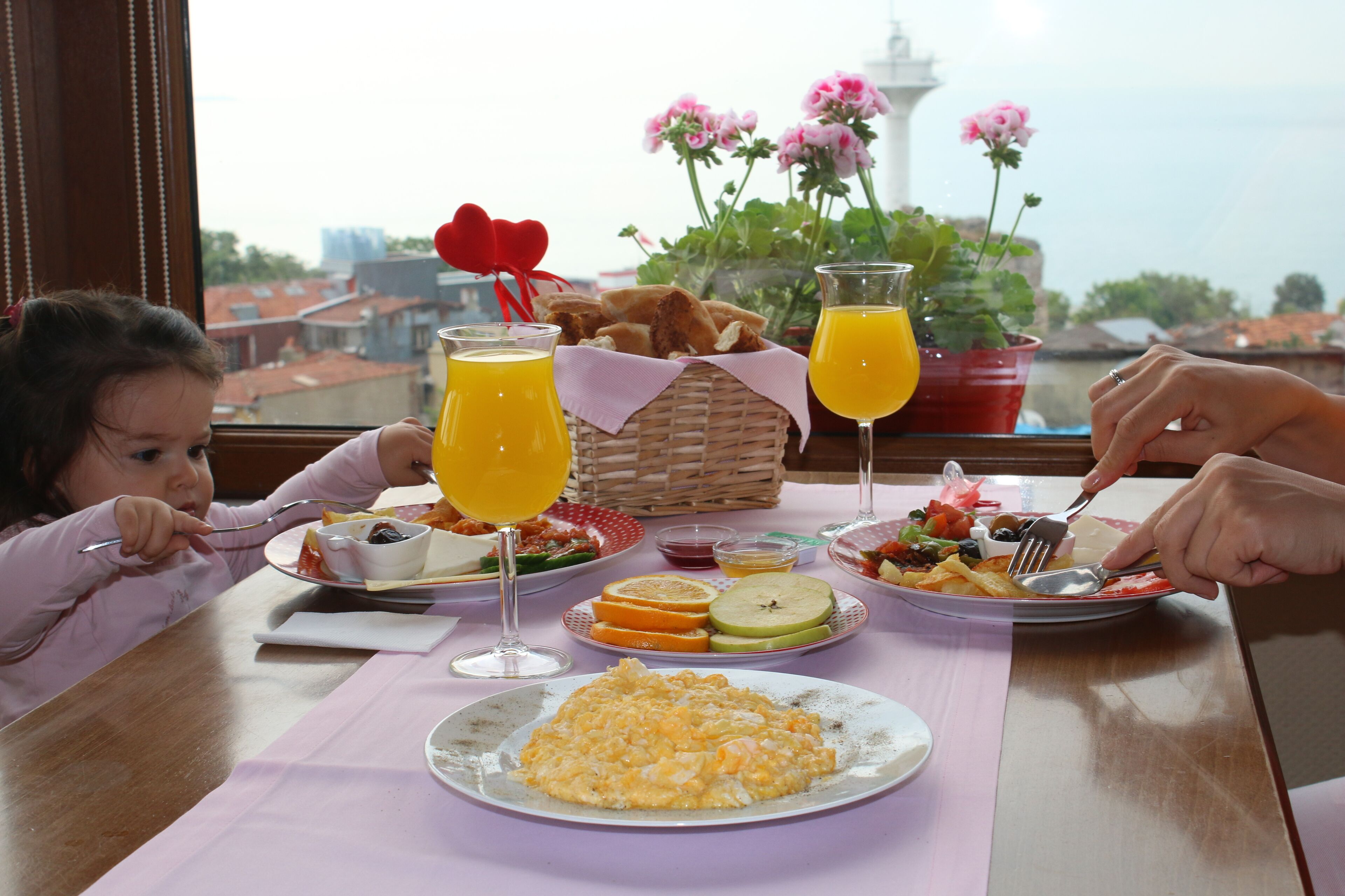 Une table à manger avec des aliments pour le petit-déjeuner, notamment des assiettes de nourriture, des verres de jus d’orange et un panier de pain.