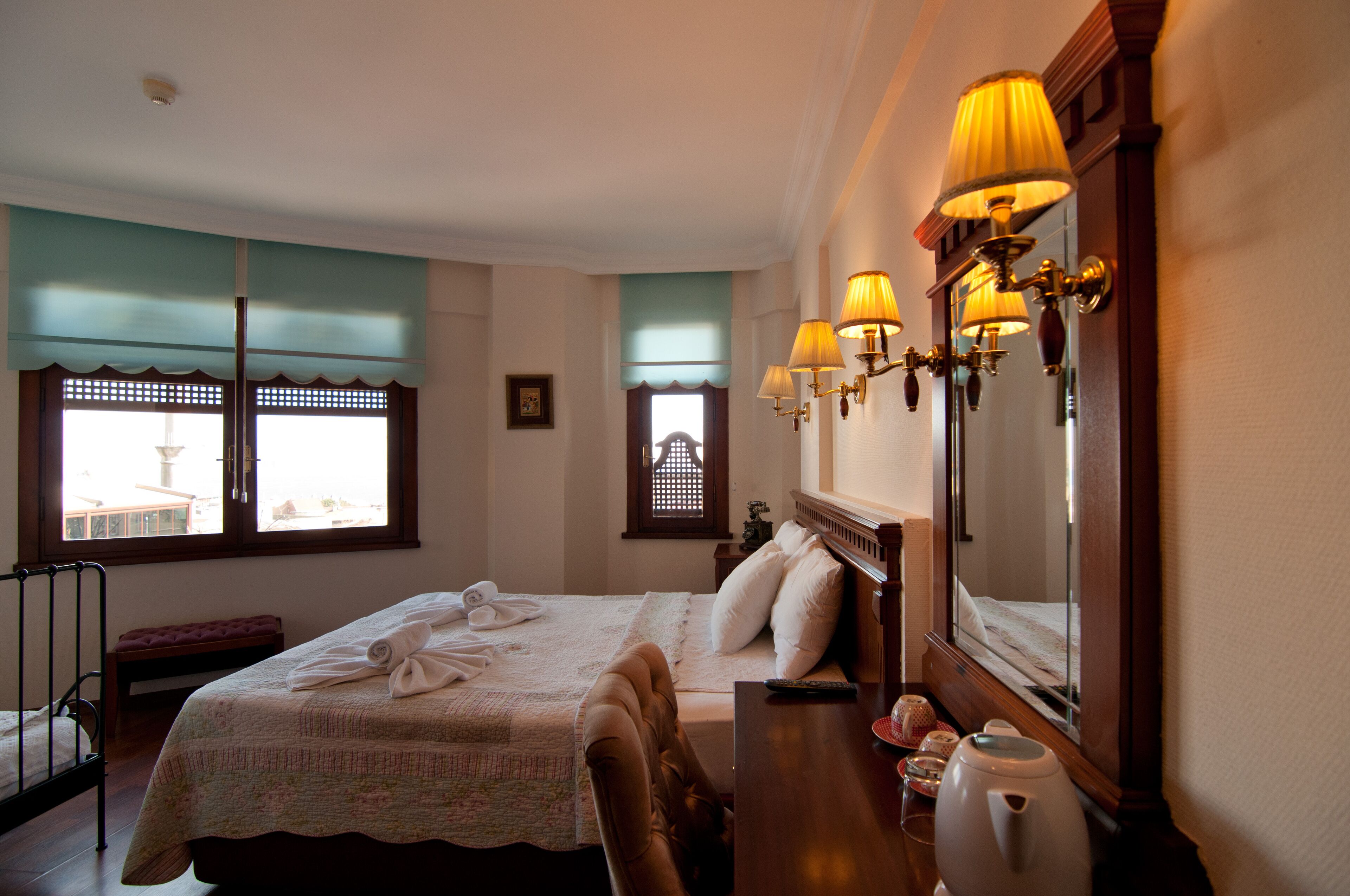 A hotel room with a bed, bedside table, lamp, and a view of the outside.