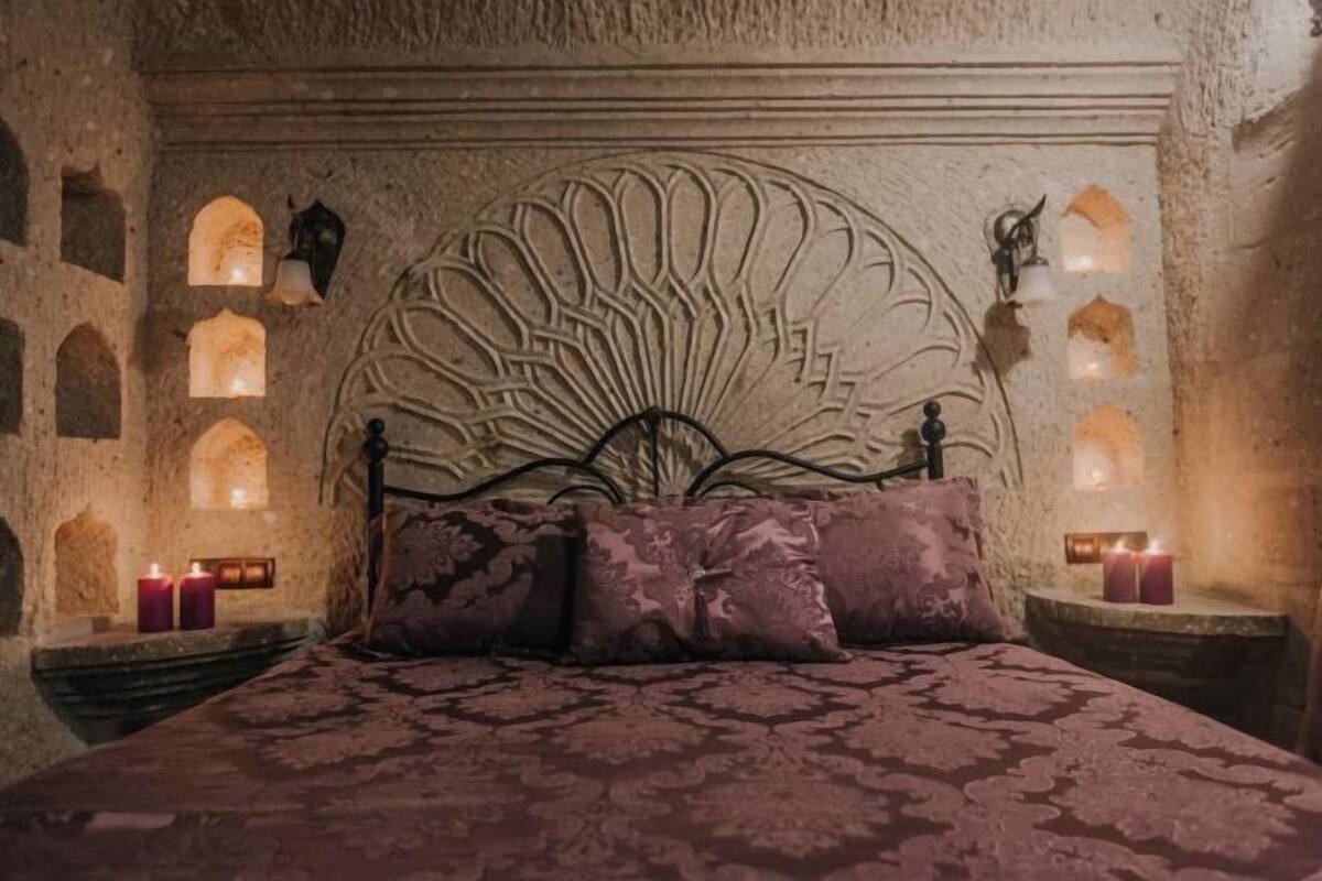 A room with a stone wall, a bed with a patterned bedspread, and candles on the nightstands.