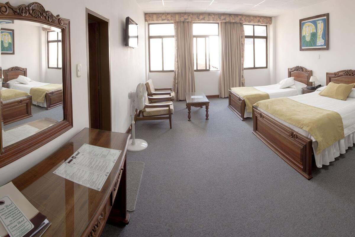 A hotel room with two beds, a desk, a chair, a small table, and a mirror.