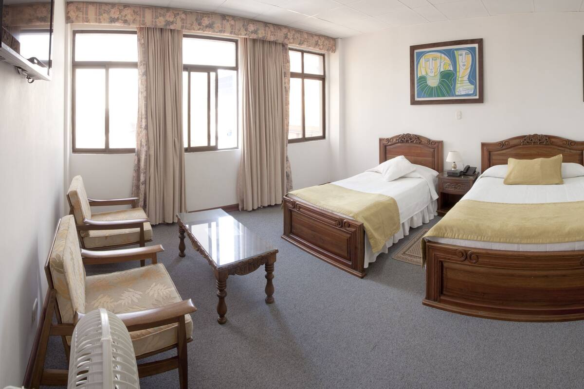 A hotel room with two wooden beds, a desk, a chair, a television, and two paintings on the wall.
