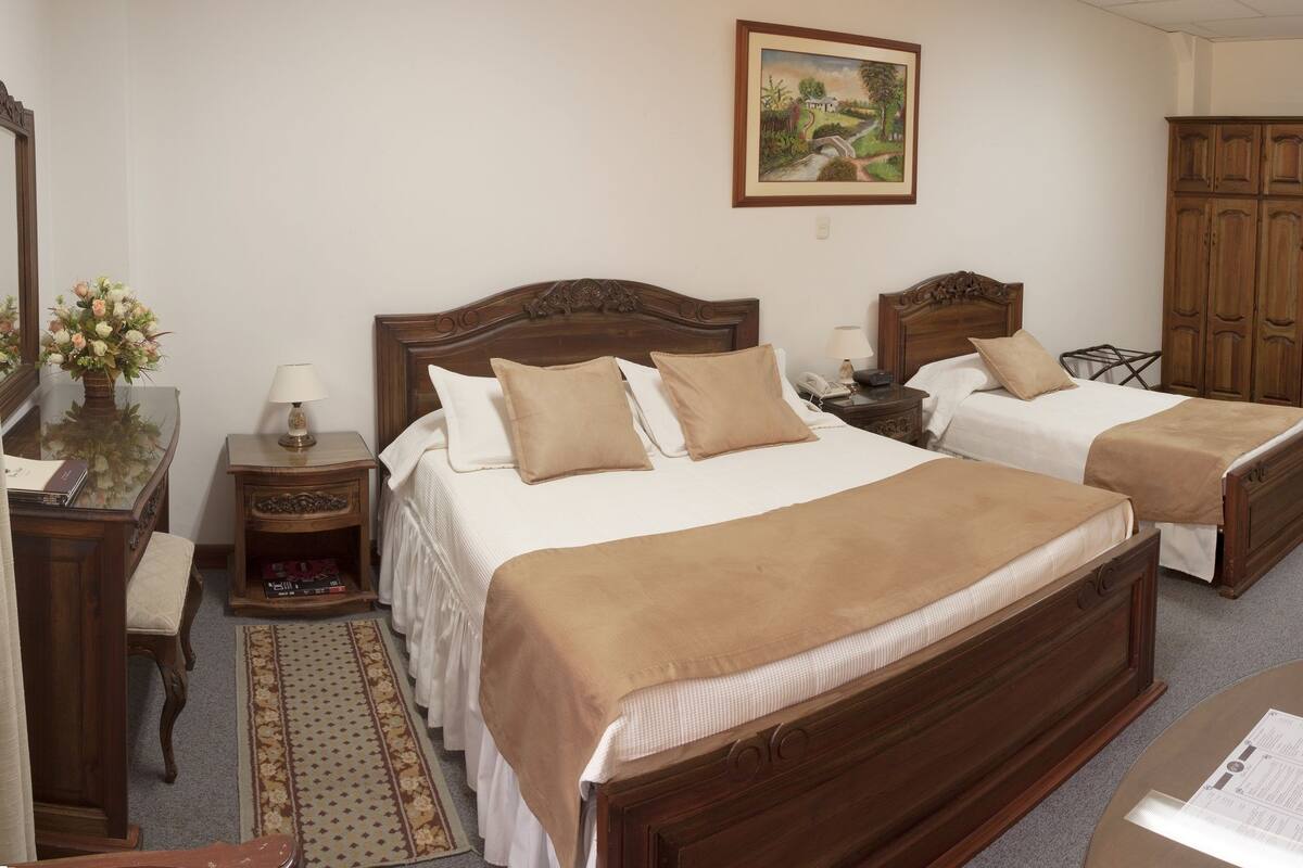 A hotel room with two wooden beds, a sofa, a TV, and a desk with a lamp.