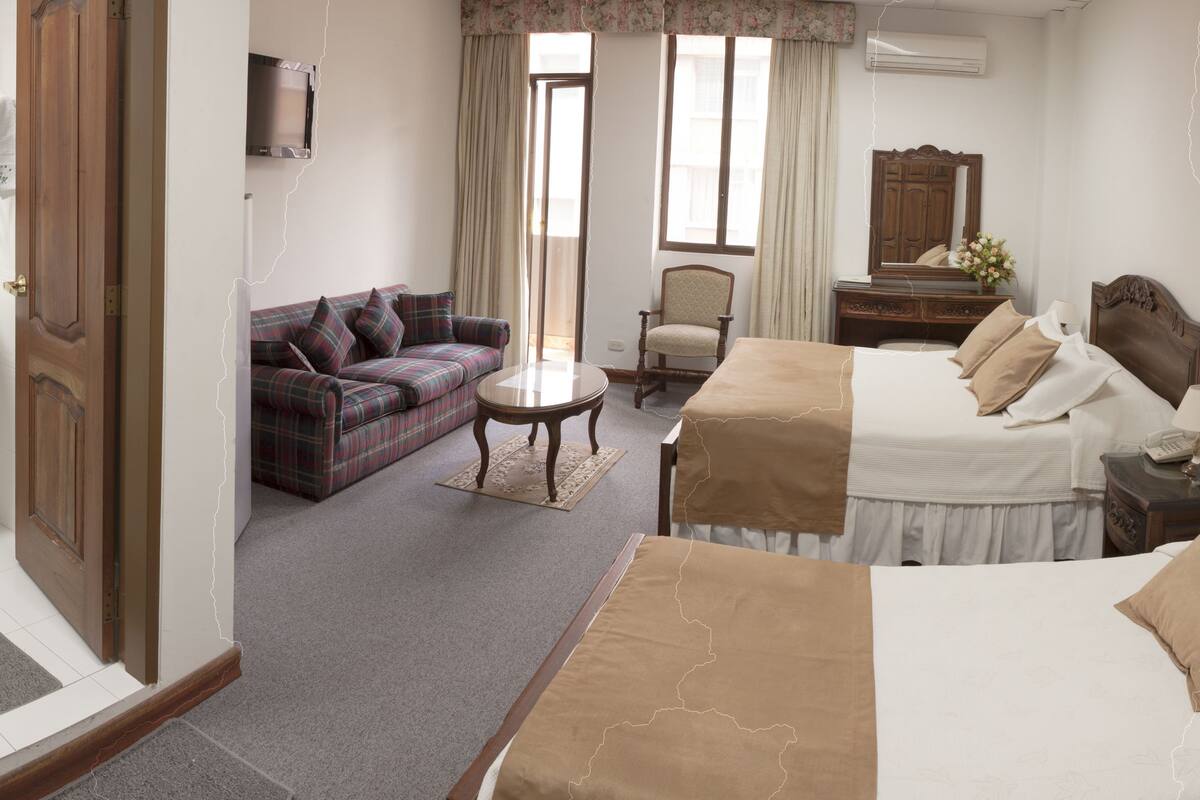 A hotel room with two beds, a sofa, a chair, a small table, and a TV.