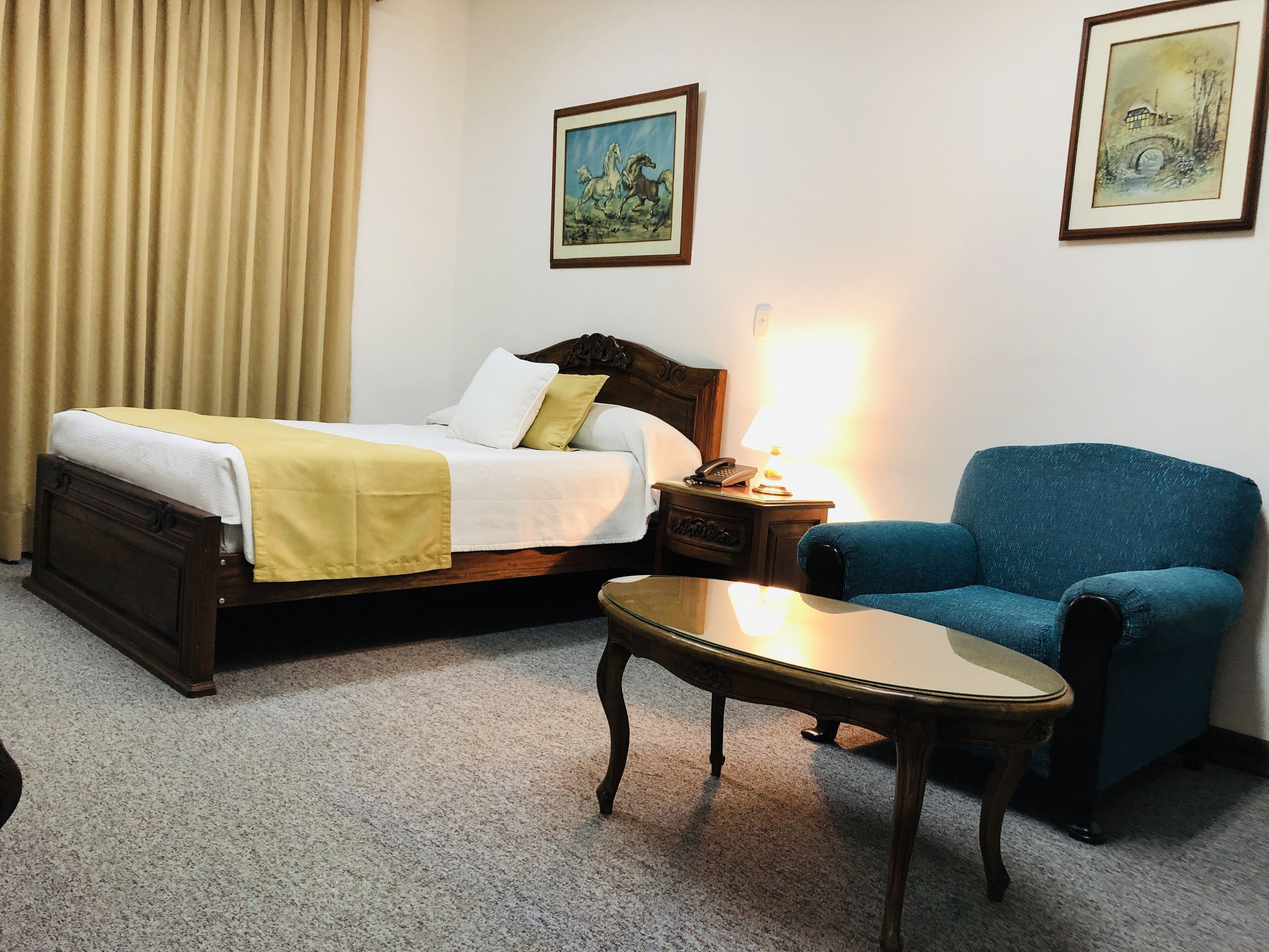 A hotel room with a bed, a bedside table, a chair, and two framed pictures on the wall.