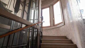 A staircase with a glass railing and a view of the outside through a window. - Palazzina Fortuny (Venice)