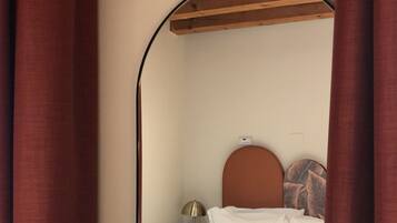 A bedroom with a bed, a nightstand, a lamp, and a wall-mounted shelf.