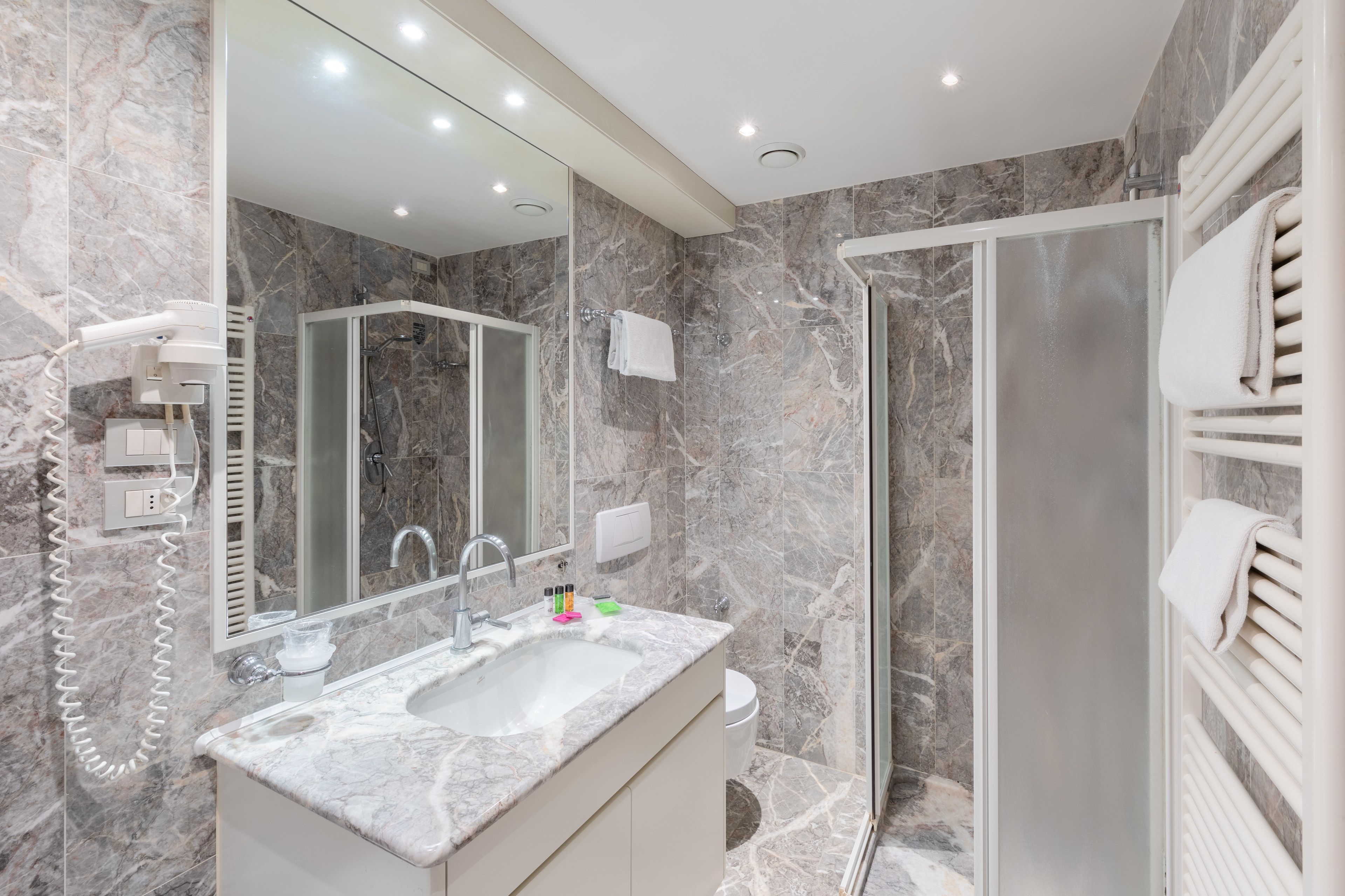 A modern bathroom with a marble sink, a glass shower enclosure, and a large mirror.