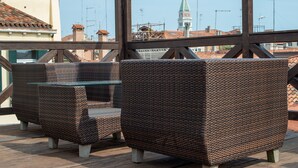 Wicker furniture on a balcony with a view of buildings and a tower in the background. - Palazzina Fortuny (Venice)