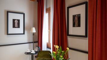 Une chambre d’hôtel avec un fauteuil vert, une petite table avec des tasses, une lampe et deux tableaux encadrés au mur.