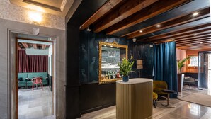 A modern lobby with a reception desk, a large mirror, and a seating area with a sofa and chairs. - Palazzina Fortuny (Venice)