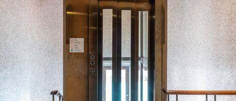 An elevator entrance with a metallic finish, glass panels, and a ceiling with recessed lighting.