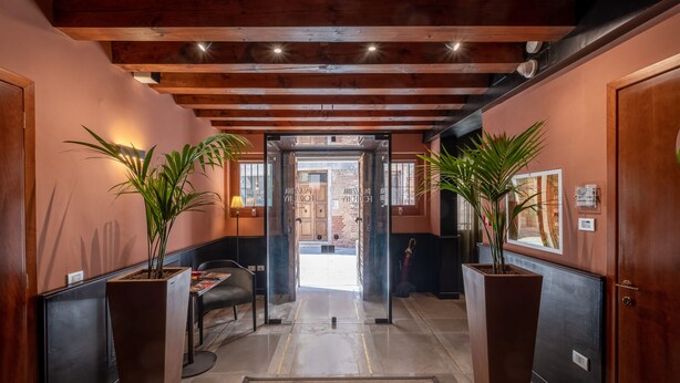 A hallway with wooden beams, potted plants, and a door leading to a room. - Palazzina Fortuny (Venice)