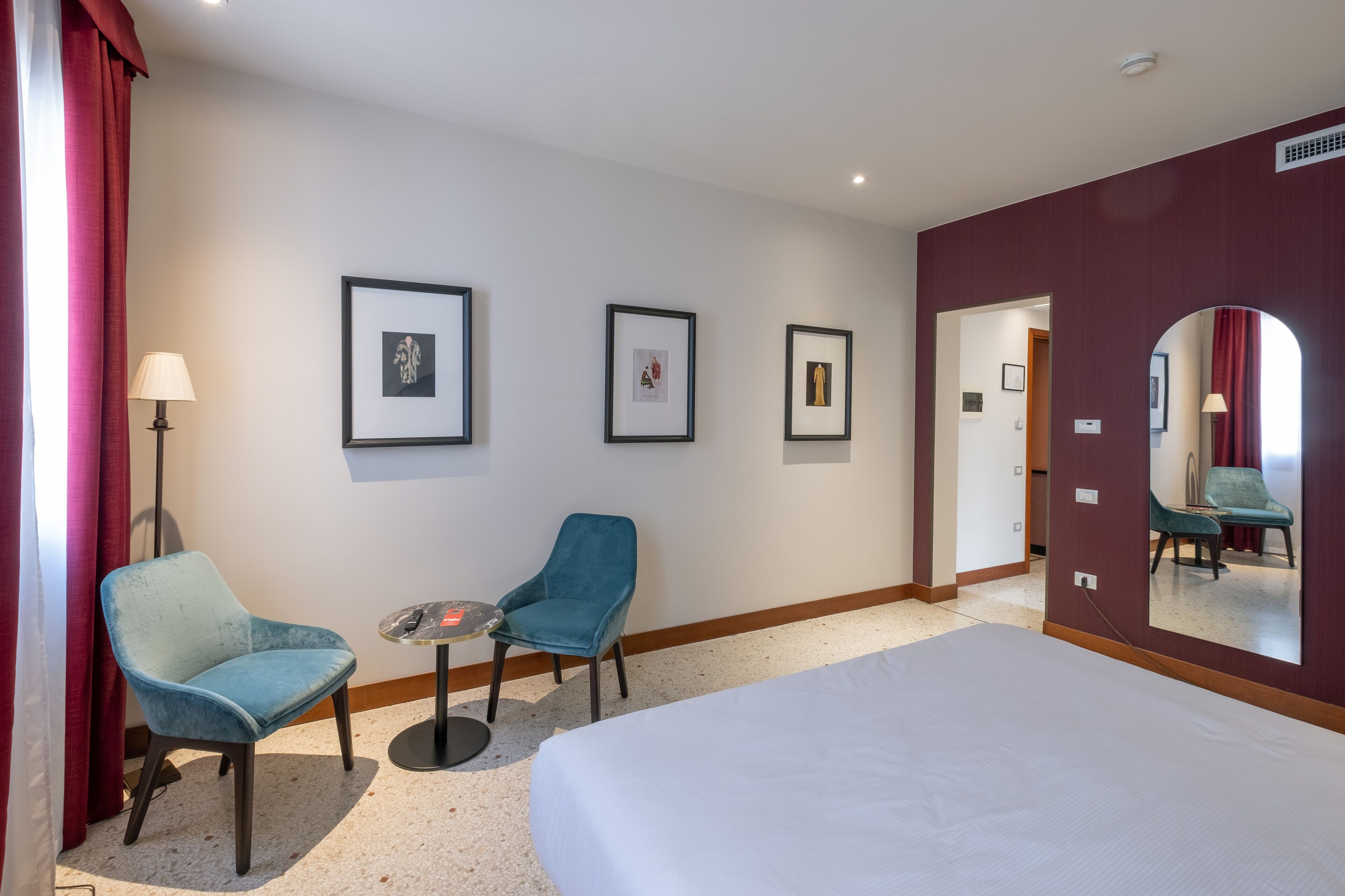 A hotel room with a bed, two chairs, a small table, and framed pictures on the wall.