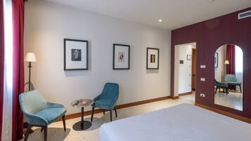 Een hotelkamer met een bed, twee stoelen, een klein tafeltje en foto's in lijsten aan de muur.