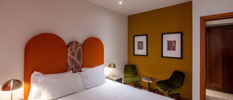 Habitación de hotel con una cama grande, dos sillones, una mesita y cuadros en la pared.