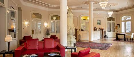 A spacious lobby with red seating, a grand staircase, and ornate ceiling details.