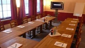 A conference room with long tables, chairs, a whiteboard, and a television screen.