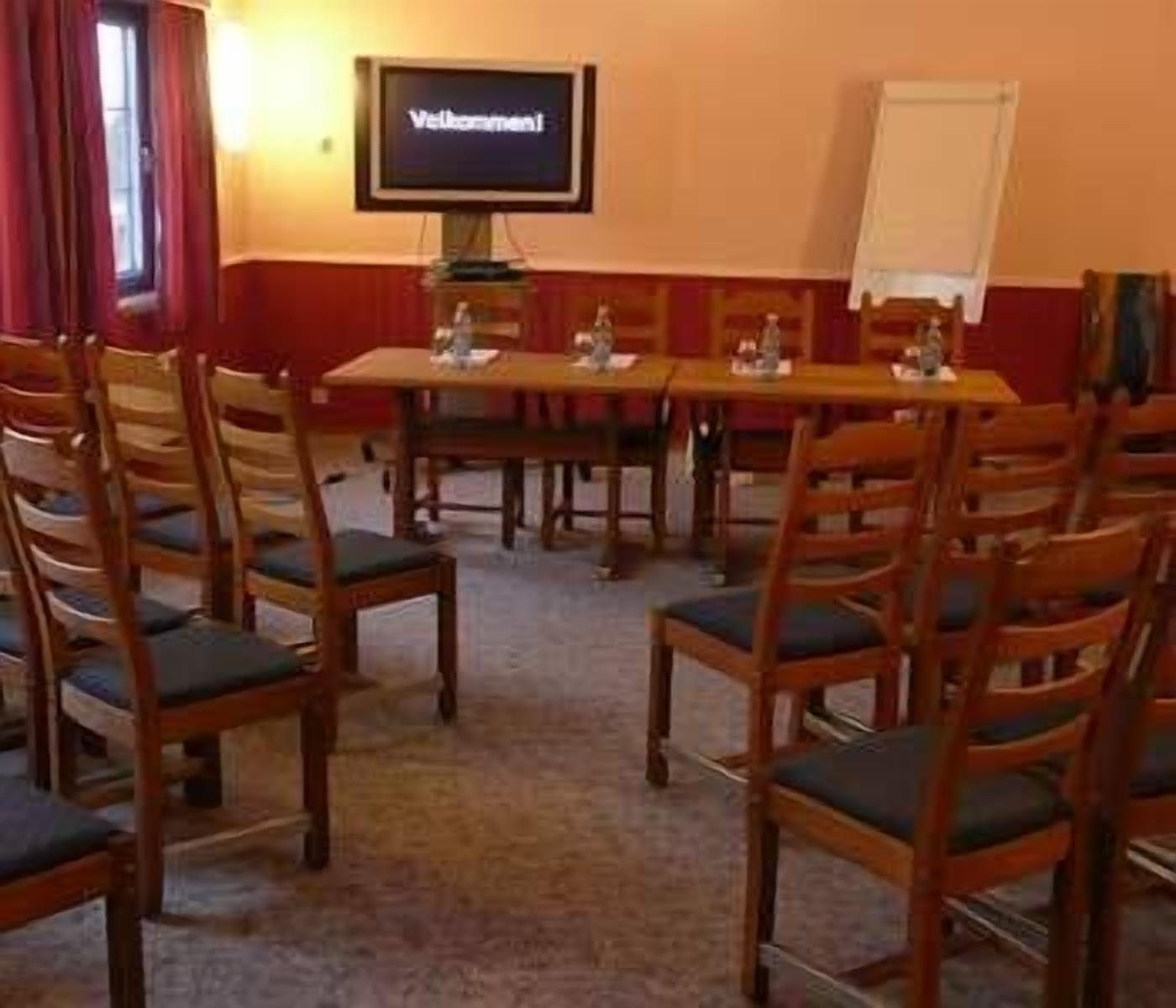 Un salón de conferencias con una larga mesa y numerosas sillas, una pantalla de televisión y una pizarra.