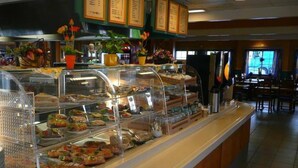 A buffet area with various food items displayed in glass cases, a menu board above, and a seating area in the background.