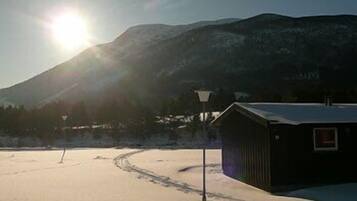 A snow-covered landscape with a mountain in the background and a small building with a sloped roof.