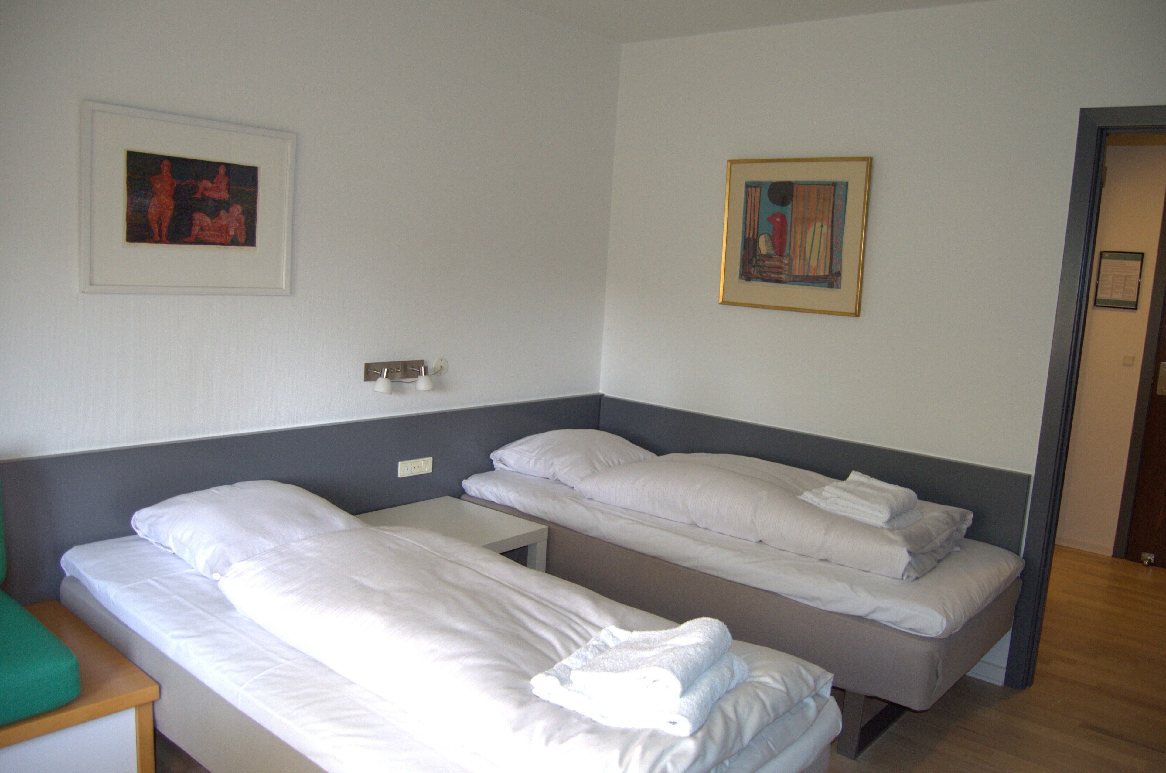 Una habitación de hotel con dos camas individuales, una mesita y dos cuadros en las paredes.