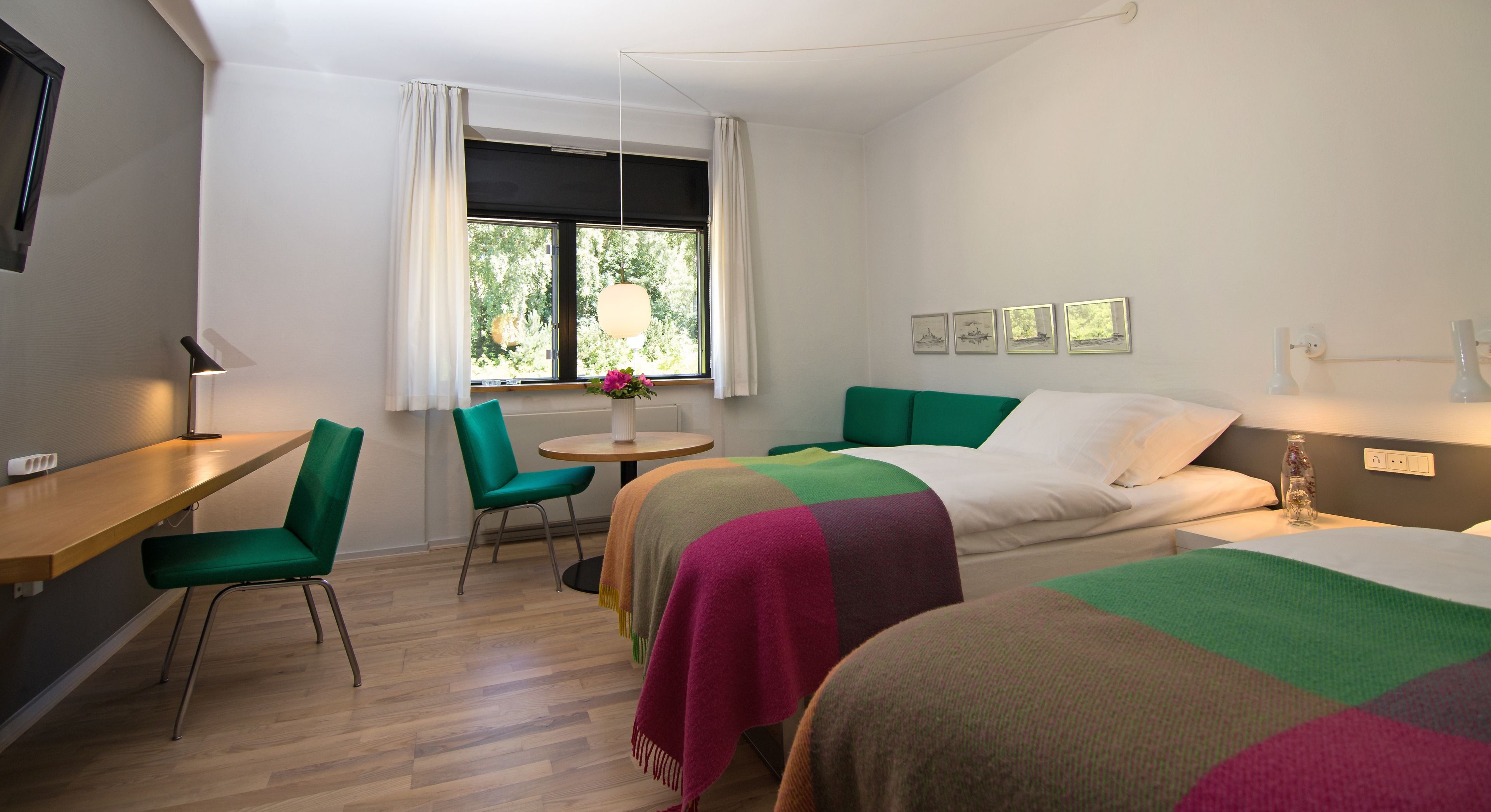 A hotel room with two beds, a desk, a chair, and a window with curtains.