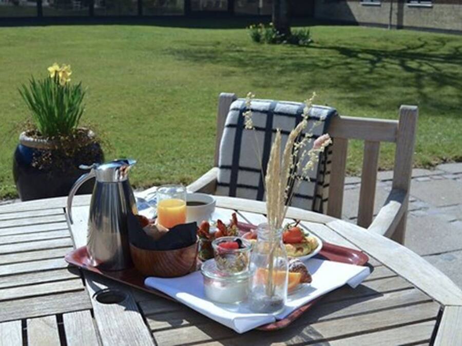 A breakfast tray with coffee, orange juice, and pastries on a wooden table outdoors.