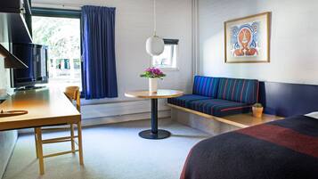 Et hotelværelse med en seng, en sofa, et lille bord med en vase blomster, et fjernsyn og et vindue med gardiner.