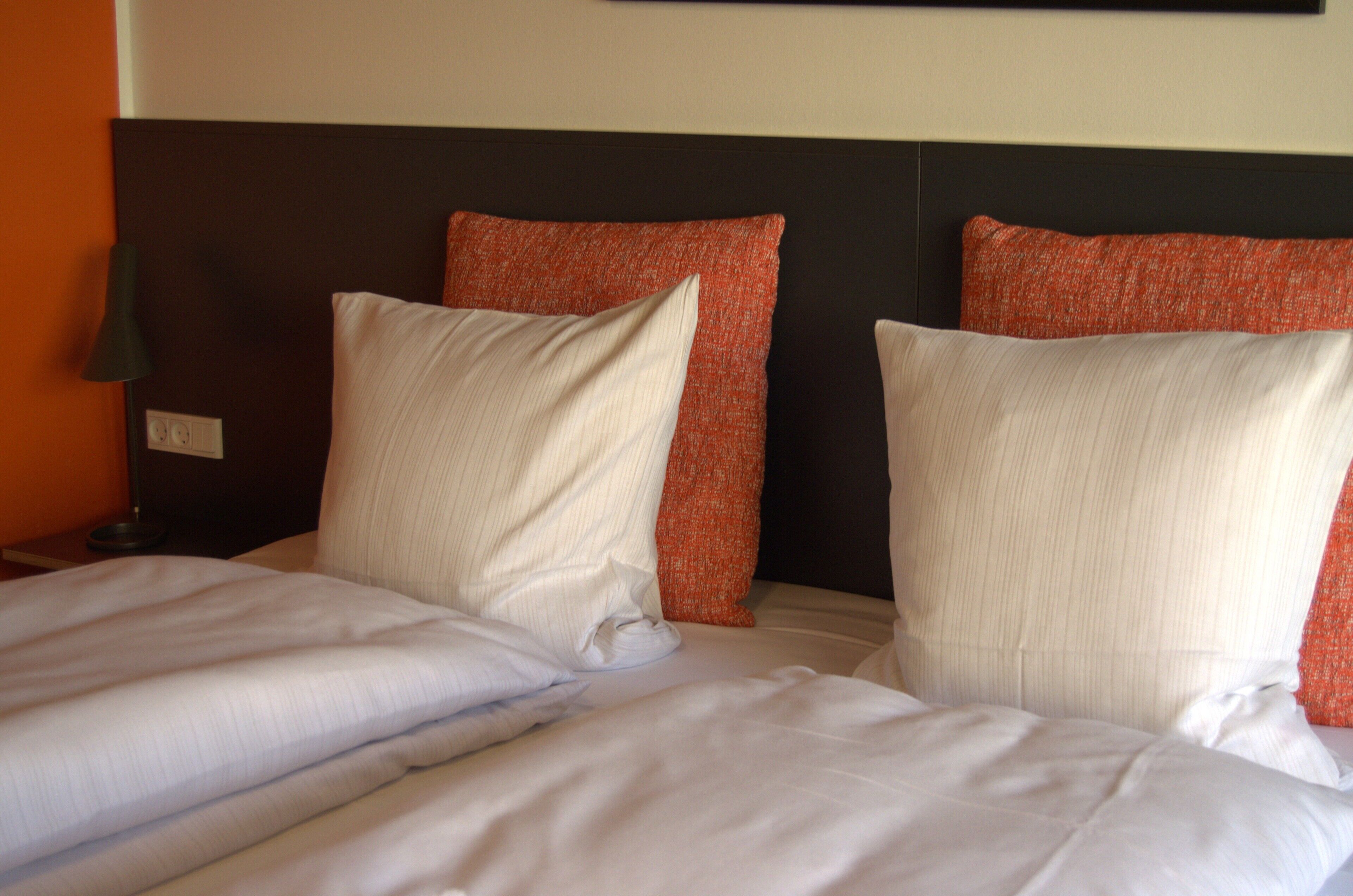 Una habitación de hotel con una cama, dos almohadas, una mesita de noche y una lámpara.