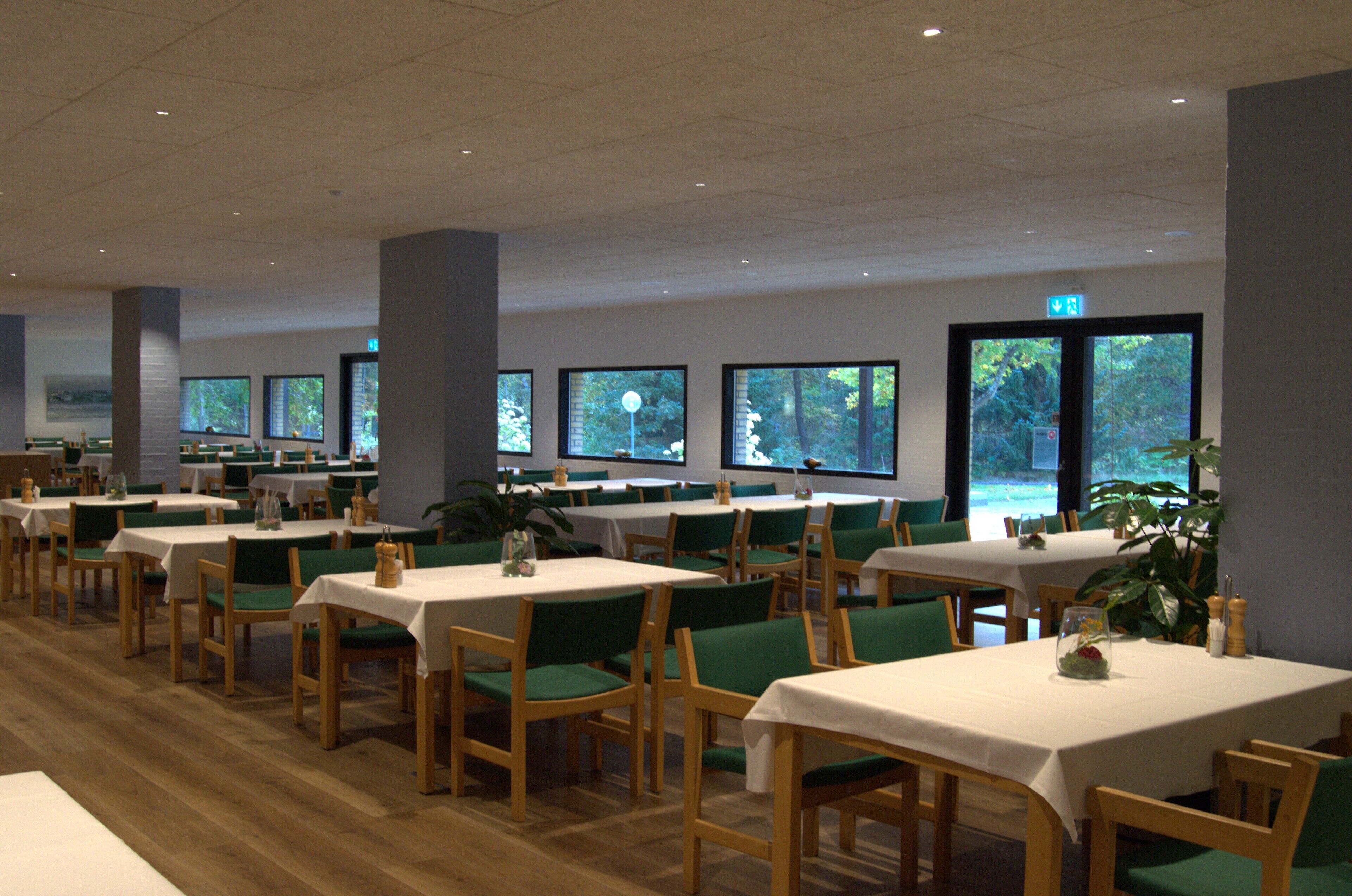 A dining area with multiple tables and chairs, large windows, and a view of trees outside.